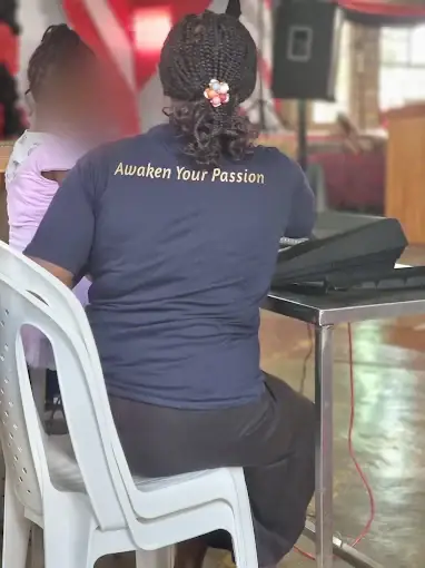 A trainer in an Awaken Your Passion tee teaching a child at the keyboard — Concerto Music Place, Kikuyu